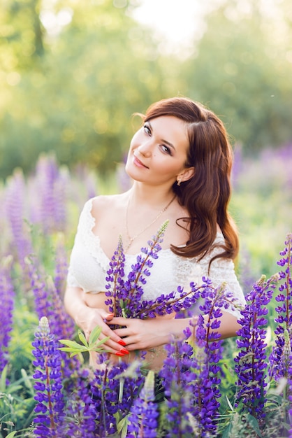 Retrato de uma mulher bonita em um campo com flores roxas. Foto ensolarada de verão com uma jovem morena em tremoço roxo