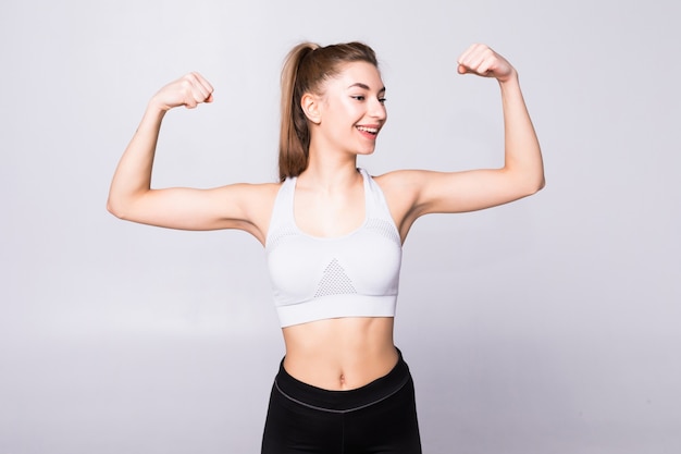 Retrato de uma mulher bonita fitness mostrando seu bíceps isolado em uma parede branca