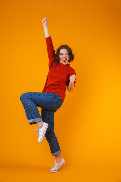 Foto retrato de uma mulher bonita jovem feliz emocional animado posando isolado sobre a parede amarela faz gesto de vencedor.