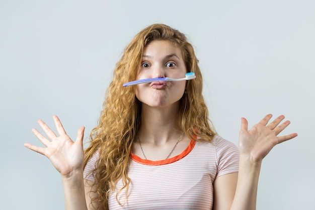 Retrato de uma mulher bonita sorridente com cabelo encaracolado vermelho segurando a escova de dentes isolada em um fundo branco