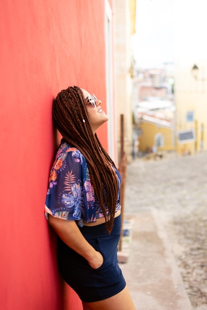 Retrato de uma mulher bonita usando óculos de sol com tranças no cabelo apoiada contra uma parede vermelha Pelourinho Brasil