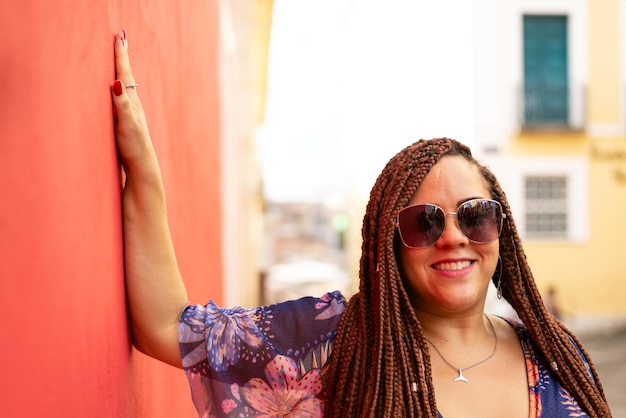 Retrato de uma mulher bonita usando óculos de sol com tranças no cabelo apoiada contra uma parede vermelha Pelourinho Brasil