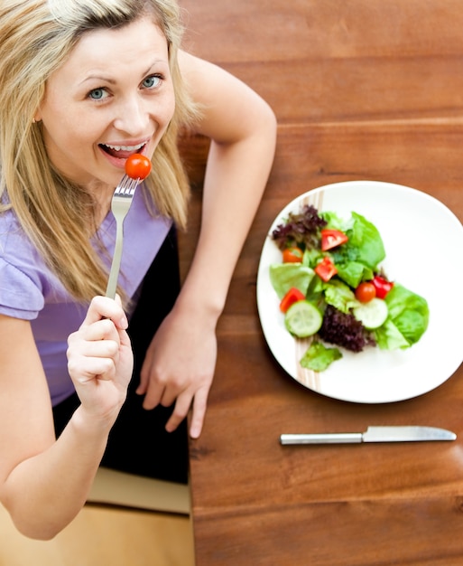 Retrato de uma mulher brilhante comendo uma salada na sala de estar