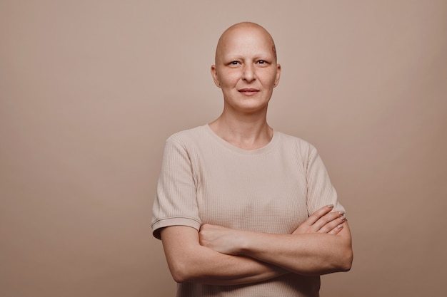 Retrato de uma mulher careca confiante em tons quentes, olhando para a câmera enquanto posa contra um fundo bege mínimo no estúdio, alopecia e conscientização do câncer, copie o espaço