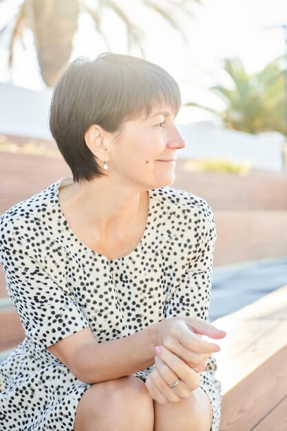 Retrato de uma mulher caucasiana feliz de 50 anos sentada e sorrindo no parque no banco, uma senhora real saudável e adulta