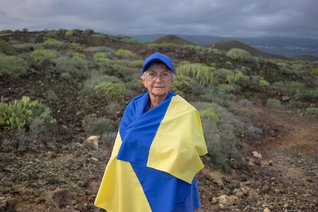 Retrato de uma mulher caucasiana sênior séria olhando para a câmera com a bandeira ucraniana nas costas Queremos liberdade para o povo ucraniano Sem guerra, queremos paz