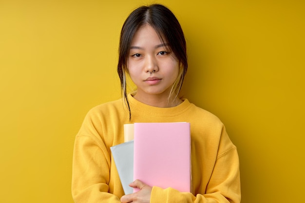 Retrato de uma mulher chinesa séria segurando livros com confiança olhando para a câmera