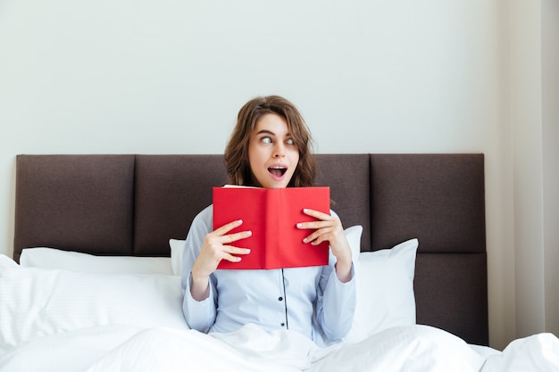 Retrato de uma mulher chocada de pijama segurando o livro