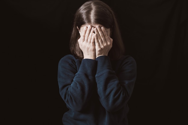 Retrato de uma mulher chorando, cobrindo o rosto com as mãos. Violência na família. Tristeza e estado depressivo da menina.