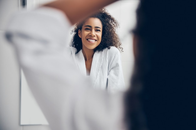 Retrato de uma mulher com cabelo encaracolado sorrindo para seu reflexo no espelho