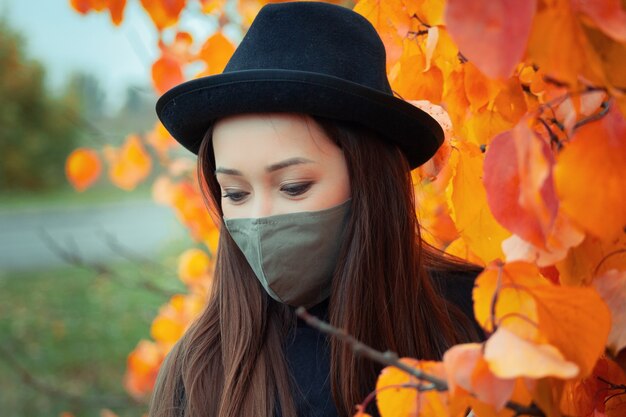 retrato de uma mulher com chapéu e máscara sobre uma árvore de outono