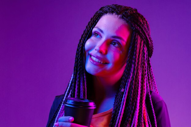 Retrato de uma mulher com longas tranças afro segurando uma xícara de café contra um fundo roxo de néon