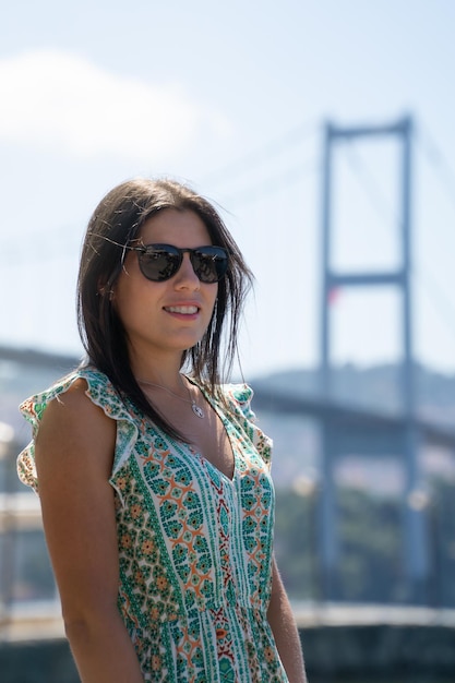 Retrato de uma mulher com óculos de sol em primeiro plano e a famosa ponte de Istambul fora de foco ao fundo