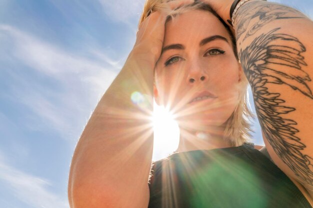 Foto retrato de uma mulher com raios de sol em cima, contra um fundo de céu azul, vista de baixo