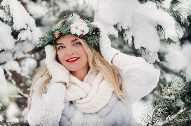 Retrato de uma mulher com roupas brancas em uma floresta fria de inverno. Menina com uma coroa na cabeça em uma floresta de inverno coberta de neve