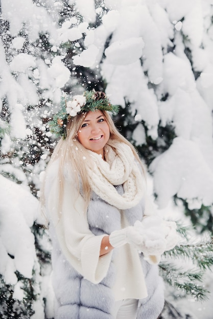 Retrato de uma mulher com um casaco de pele branco em uma floresta fria de inverno. menina com uma coroa na cabeça em uma floresta de inverno coberto de neve.