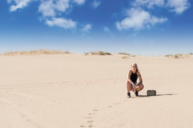 Retrato de uma mulher com um cigarro na mão de cócoras ao lado do alto-falante no deserto