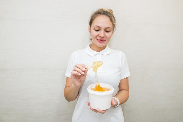 Retrato de uma mulher com um pote de pasta de açúcar para adoçarEsteticista segurando um pote de pasta de açúcar para adoçar em um fundo branco