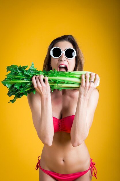 Retrato de uma mulher comendo vegetais contra um fundo amarelo