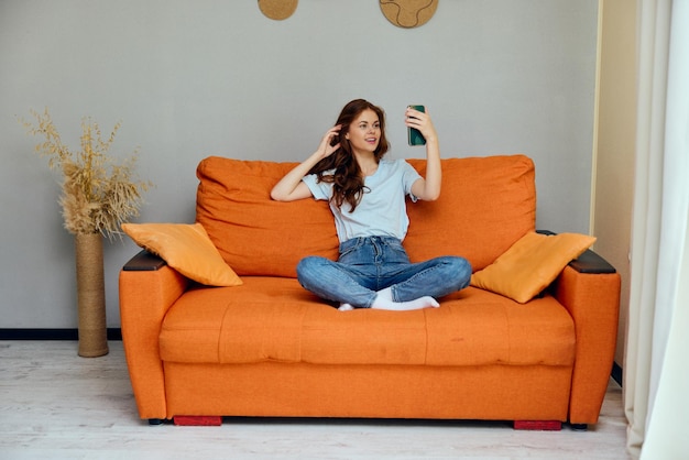 Retrato de uma mulher conversando no sofá laranja com um smartphone inalterado Foto de alta qualidade