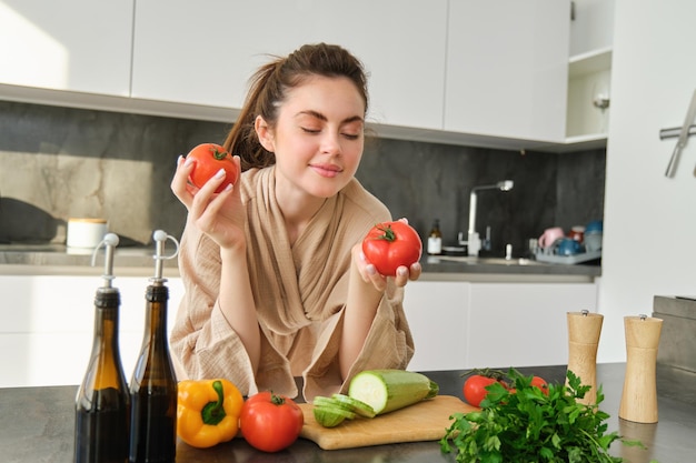 Retrato de uma mulher cozinhando em casa na cozinha segurando tomates preparando uma deliciosa refeição fresca