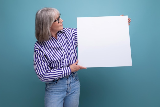 Retrato de uma mulher de cabelos grisalhos mostrando uma folha em branco com uma maquete em um fundo de estúdio brilhante