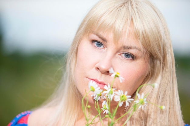 Retrato de uma mulher de meia idade com cabelos brancos segurando um buquê de margaridas do campo