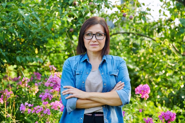 Retrato de uma mulher de meia idade confiante sorridente com braços cruzados no jardim