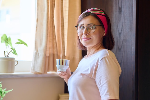 Retrato de uma mulher de meia idade em casa na cozinha com uma xícara de café