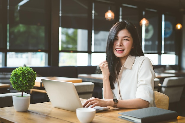 Retrato de uma mulher de negócios alegre usando um laptop na mesa de um café