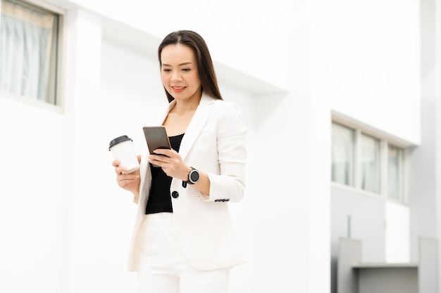 Retrato de uma mulher de negócios asiática de meia-idade segurando um telefone inteligente e um café sorrindo para a câmera