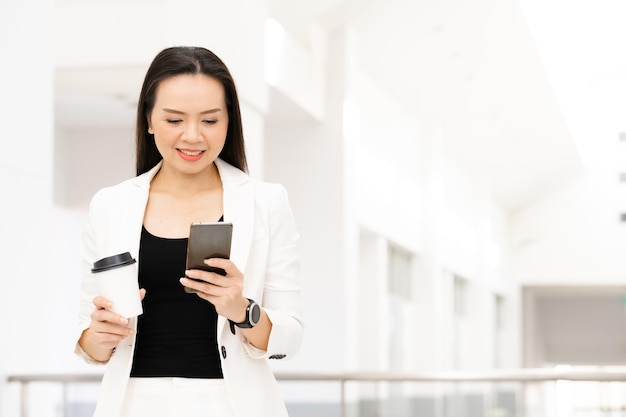 Retrato de uma mulher de negócios asiática de meia-idade segurando um telefone inteligente e um café sorrindo para a câmera