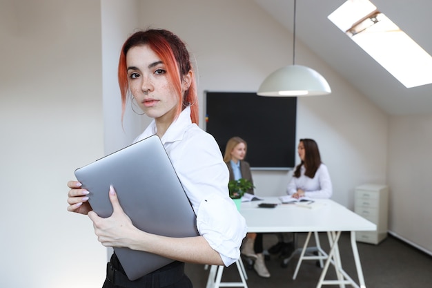 Retrato de uma mulher de negócios com um laptop no fundo de um escritório em funcionamento