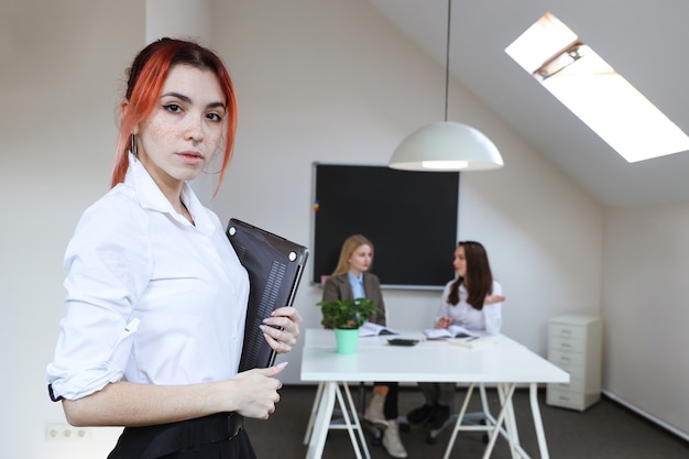 Retrato de uma mulher de negócios com um laptop no fundo de um escritório em funcionamento