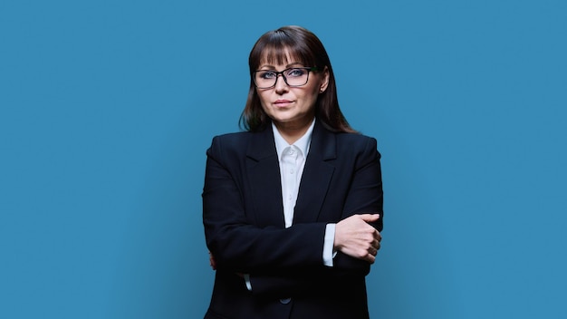 Retrato de uma mulher de negócios madura e confiante em terno preto em fundo azul