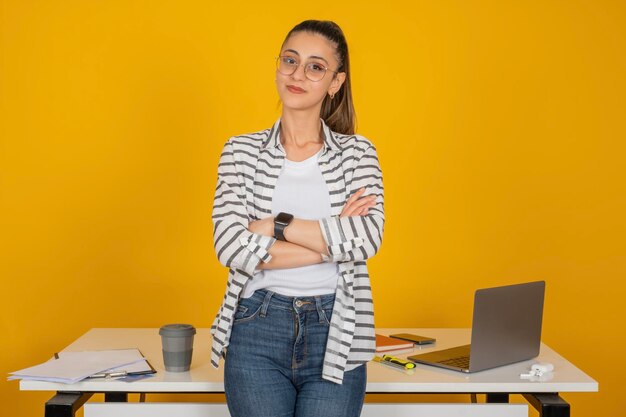 Foto retrato de uma mulher de negócios séria e confiante, morena caucasiana, inclinada para a mesa de escritório, com os braços cruzados