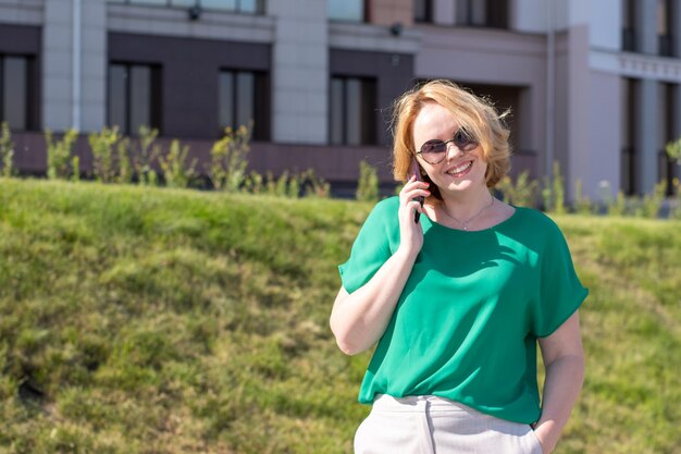 Retrato de uma mulher de negócios sorridente de meia-idade usando óculos escuros falando em um telefone celular no parque