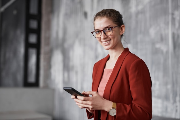 Retrato de uma mulher de negócios sorridente usando vermelho em pé contra uma parede cinza no escritório, copie o espaço