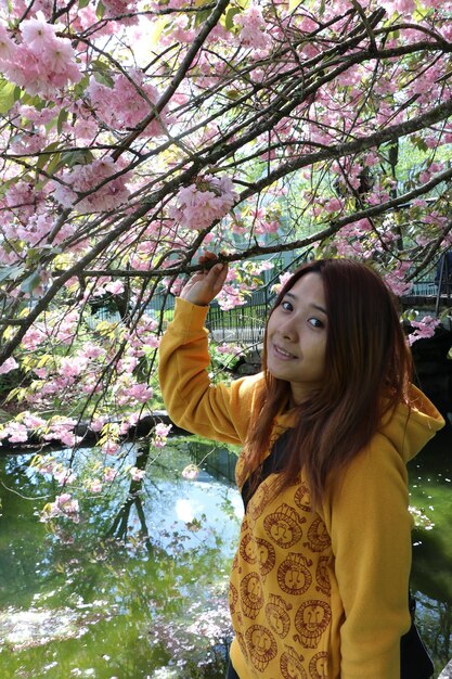 Foto retrato de uma mulher de pé junto a uma árvore de flores rosas