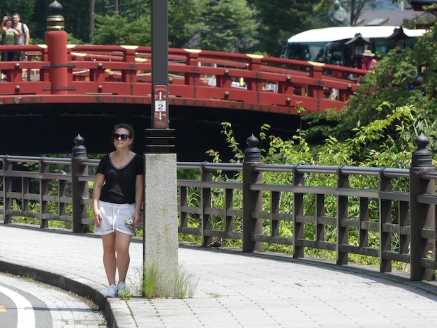 Foto retrato de uma mulher de pé por uma coluna contra uma ponte na cidade