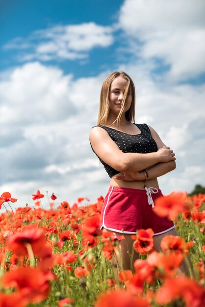 Retrato de uma mulher deslumbrante em roupas esportivas posando enquanto caminhava no incrível campo de papoulas em uma noite quente de verão. Aproveite a liberdade