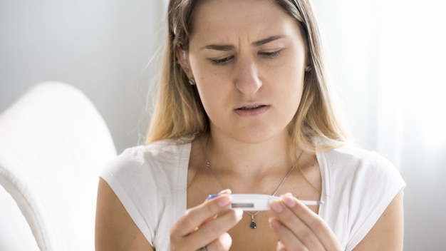 Foto retrato de uma mulher doente com gripe olhando no termômetro digital após medir a temperatura