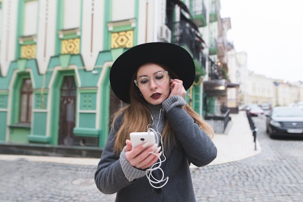 Retrato de uma mulher elegante, ouvindo música em fones de ouvido no pano de fundo de uma bela cidade velha.