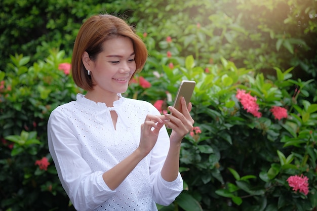 Retrato de uma mulher em pé segurando um smartphone no exterior verde