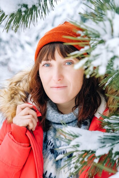 Retrato de uma mulher em uma jaqueta vermelha quente e chapéu em uma floresta de inverno nevado