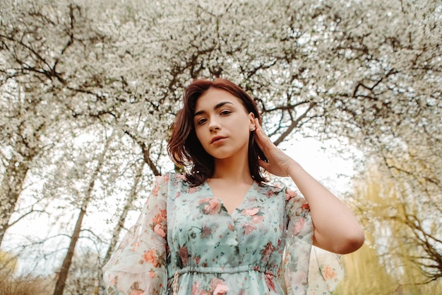 Retrato de uma mulher encantadora posando perto de flores de cerejeira de maçã florescendo flores no jardim