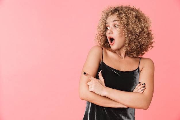 Retrato de uma mulher encaracolada chocada de 20 anos usando um vestido gritando em pé