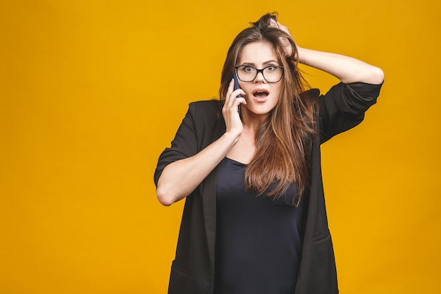 Retrato de uma mulher espantada feliz em falar casual inteligente ao telefone sobre parede amarela.