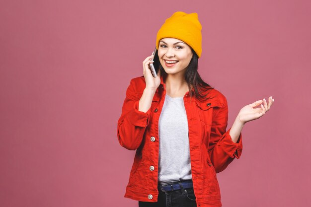 Retrato de uma mulher espantada feliz em roupas brilhantes, falando ao telefone isolado sobre a parede rosa.