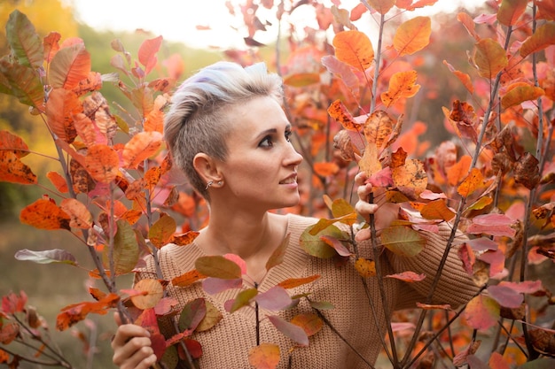 Retrato de uma mulher estilosa no fundo da floresta de outono com árvores douradas e vermelhas usando suéter bege